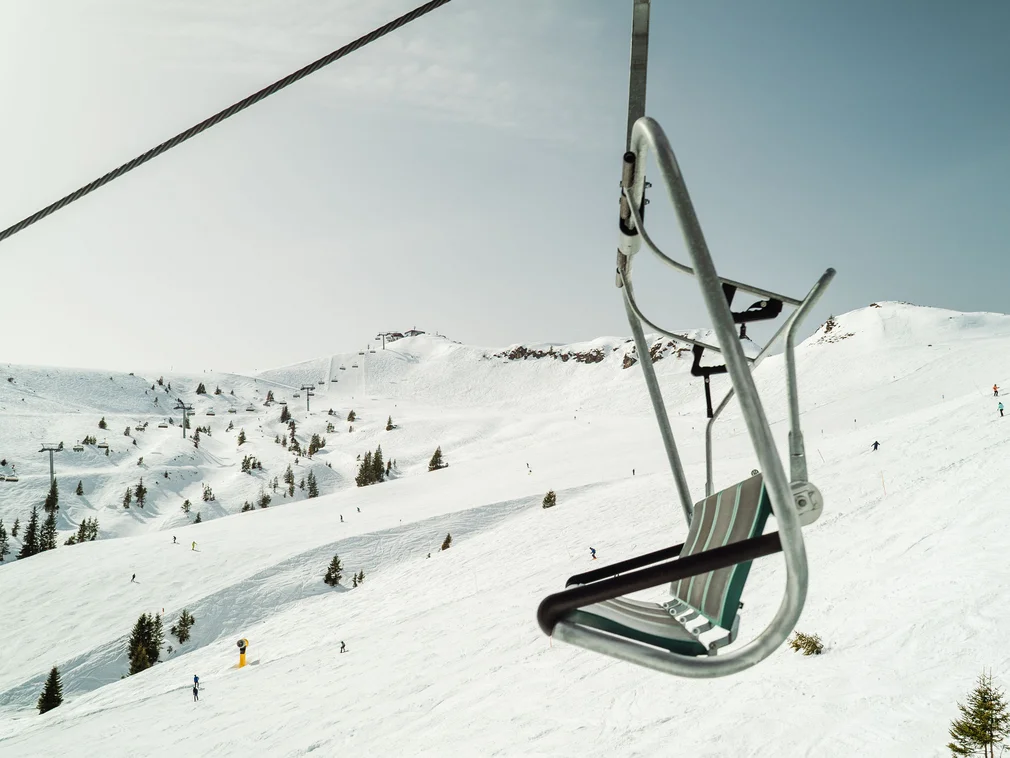 Empty ski lift on snowy mountain with skiers in the background