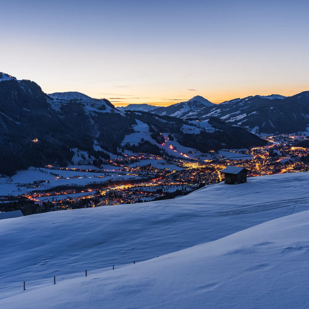 Blog Blick auf verschneite Berge und ein beleuchtetes Tal bei Sonnenuntergang