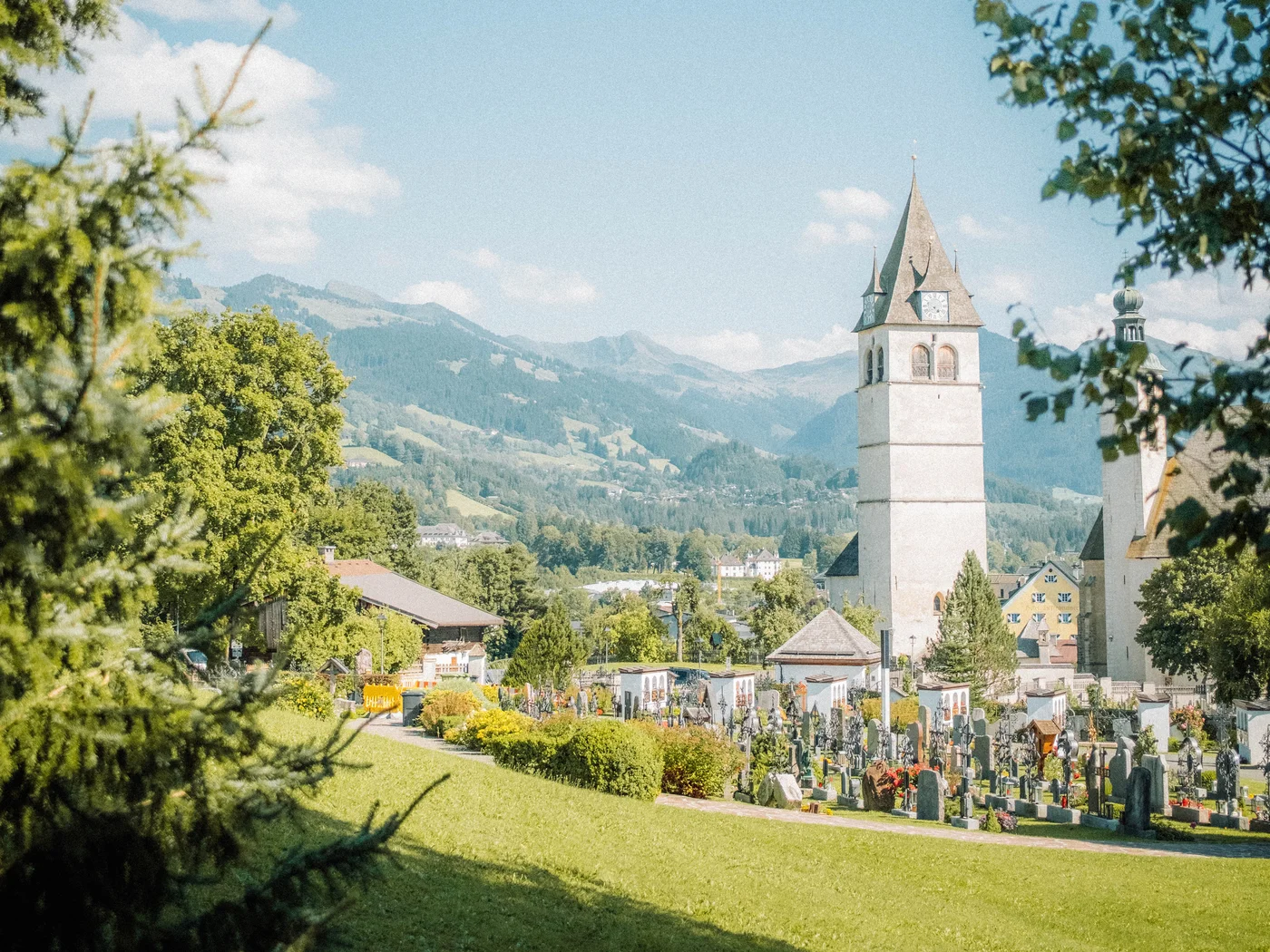 Kirchturm und Friedhof in einem grünen Tal unter blauem Himmel