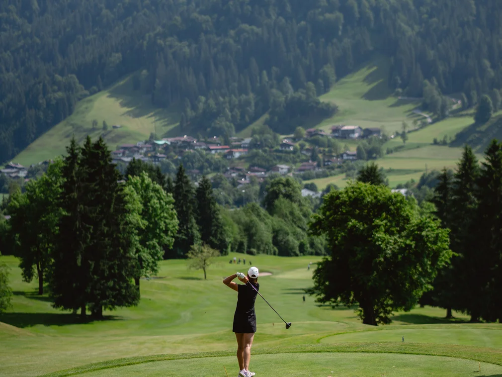 Golfer hitting ball on lush green course with mountains in the background
