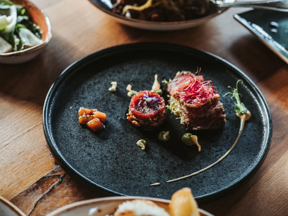 Finely plated gourmet appetizer on black plate with vegetables and sauce