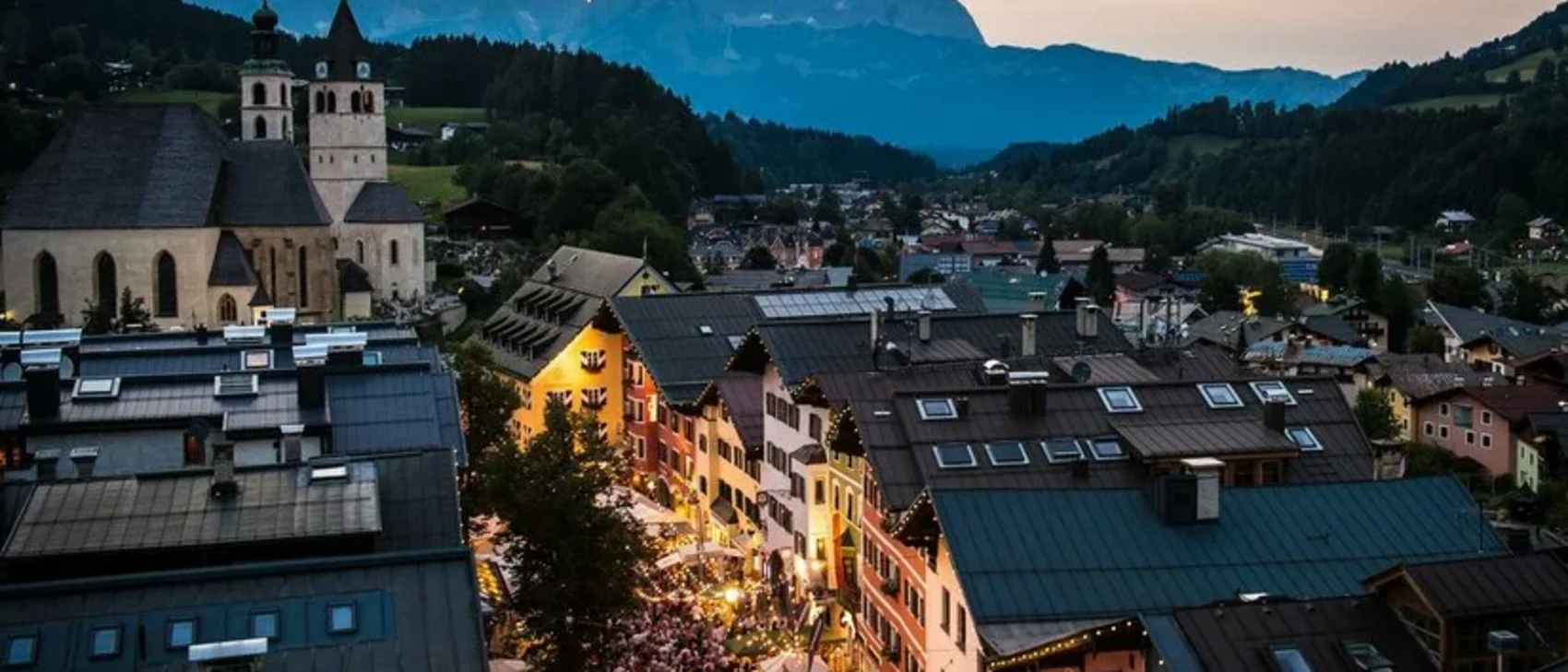 View of illuminated old town with church and mountains at dusk