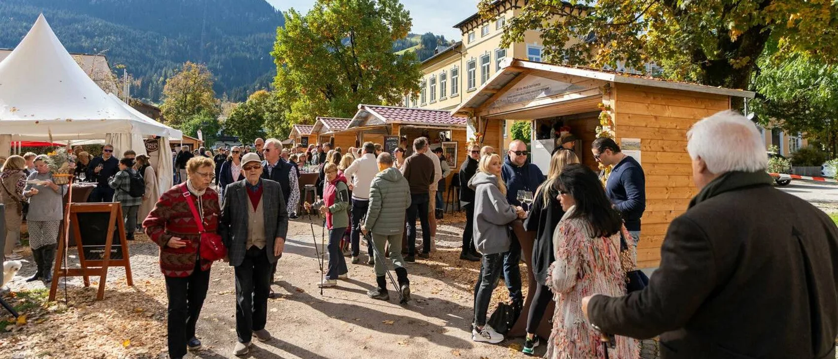 People visiting a market with wooden stalls and tents in autumn