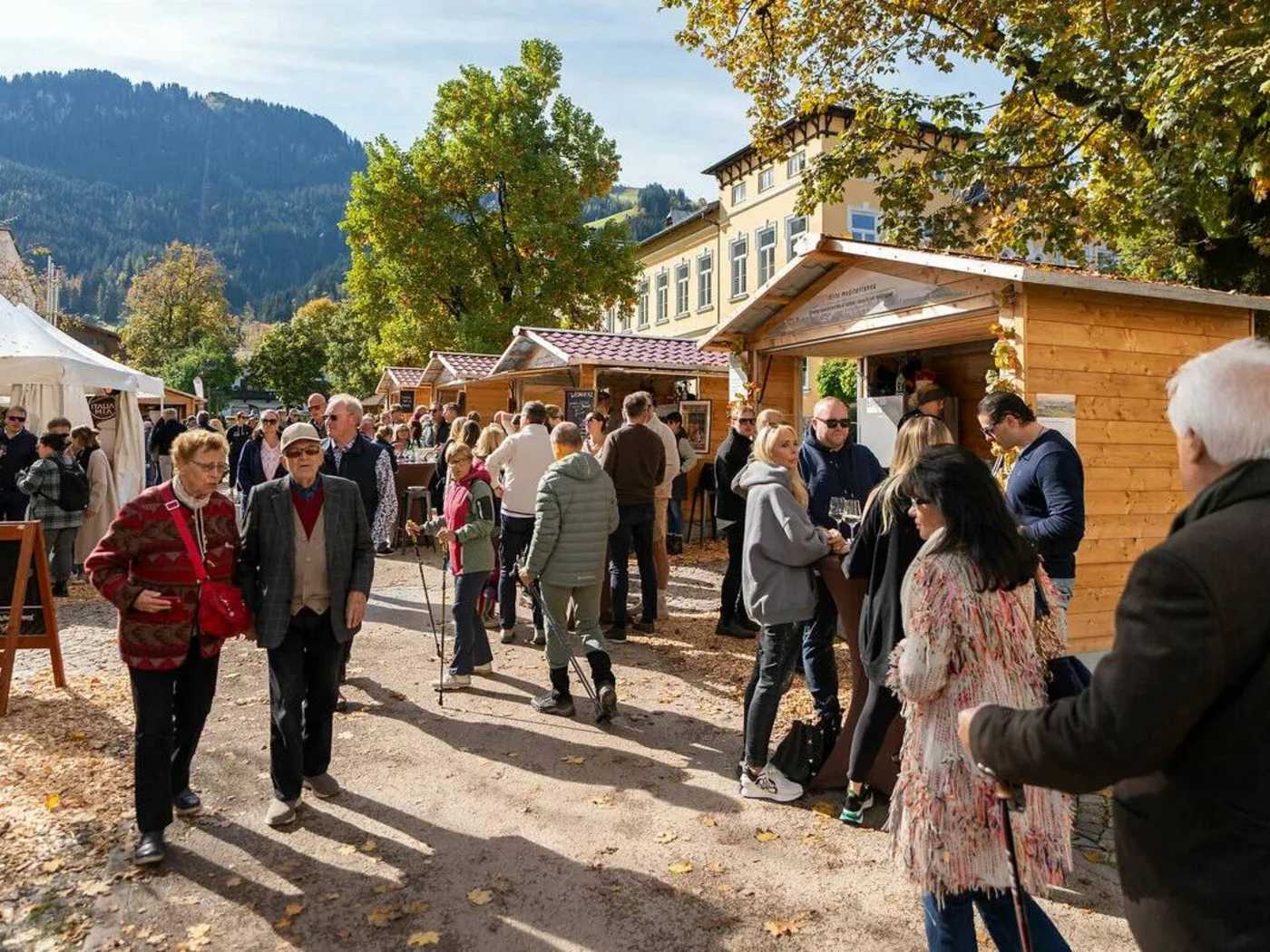 People visiting a market with wooden stalls and tents in autumn