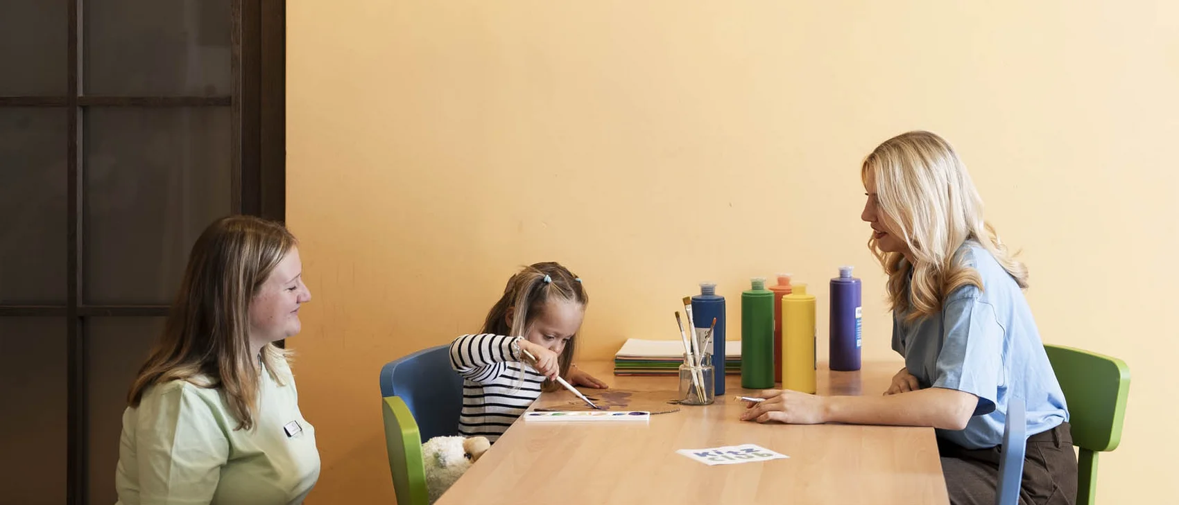Kind im Kinderclub am malen mit zwei Betreuerinnen Kind im Kinderclub am malen mit zwei Betreuerinnen