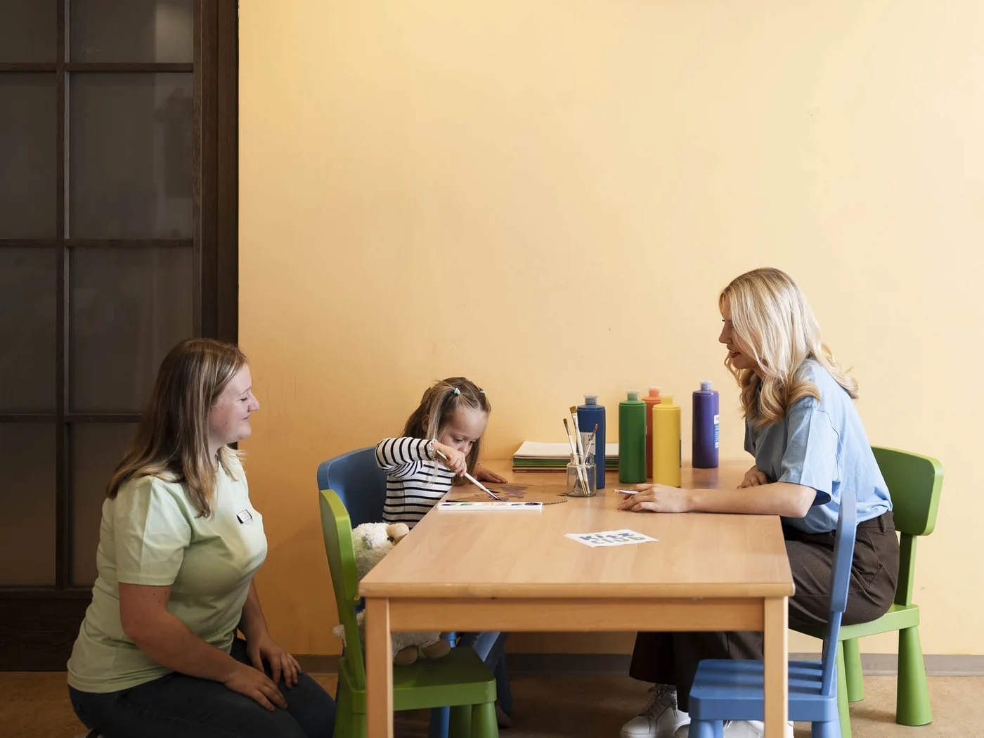 Kind im Kinderclub am malen mit zwei Betreuerinnen