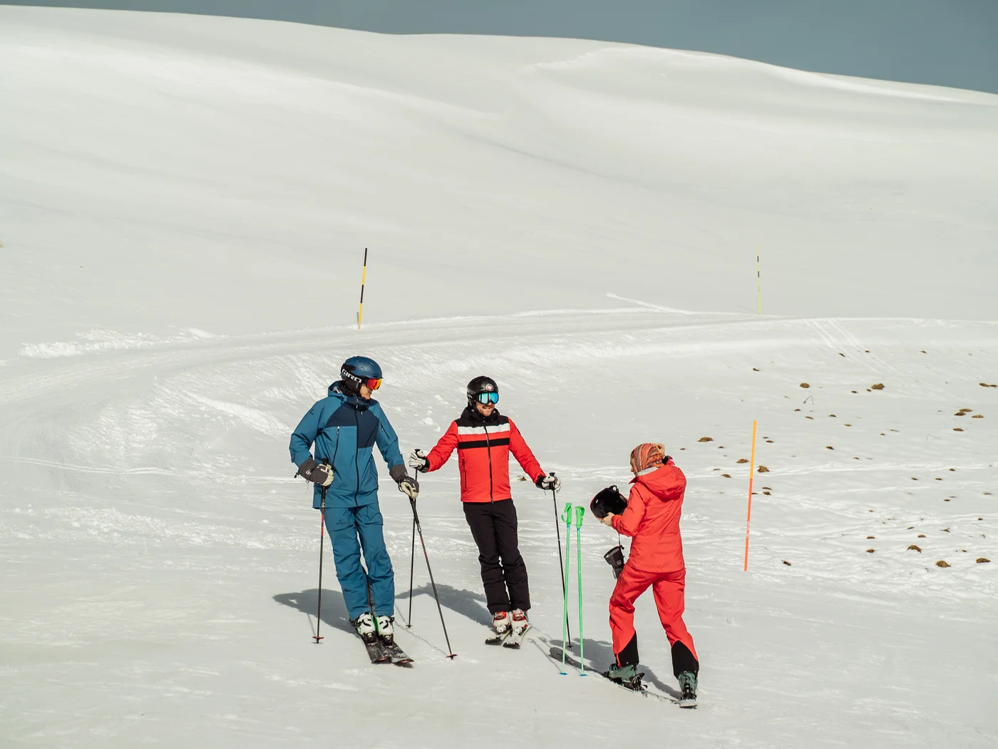 Drei Personen in Skibekleidung auf schneebedecktem Berg unter klarem Himmel