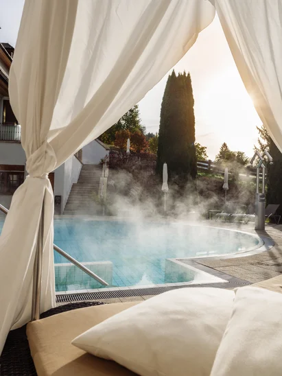 In Kitzbühel ein Hotel mit Pool, bitte. Poolbereich mit Liegestühlen und aufsteigendem Dampf vom Außenpool