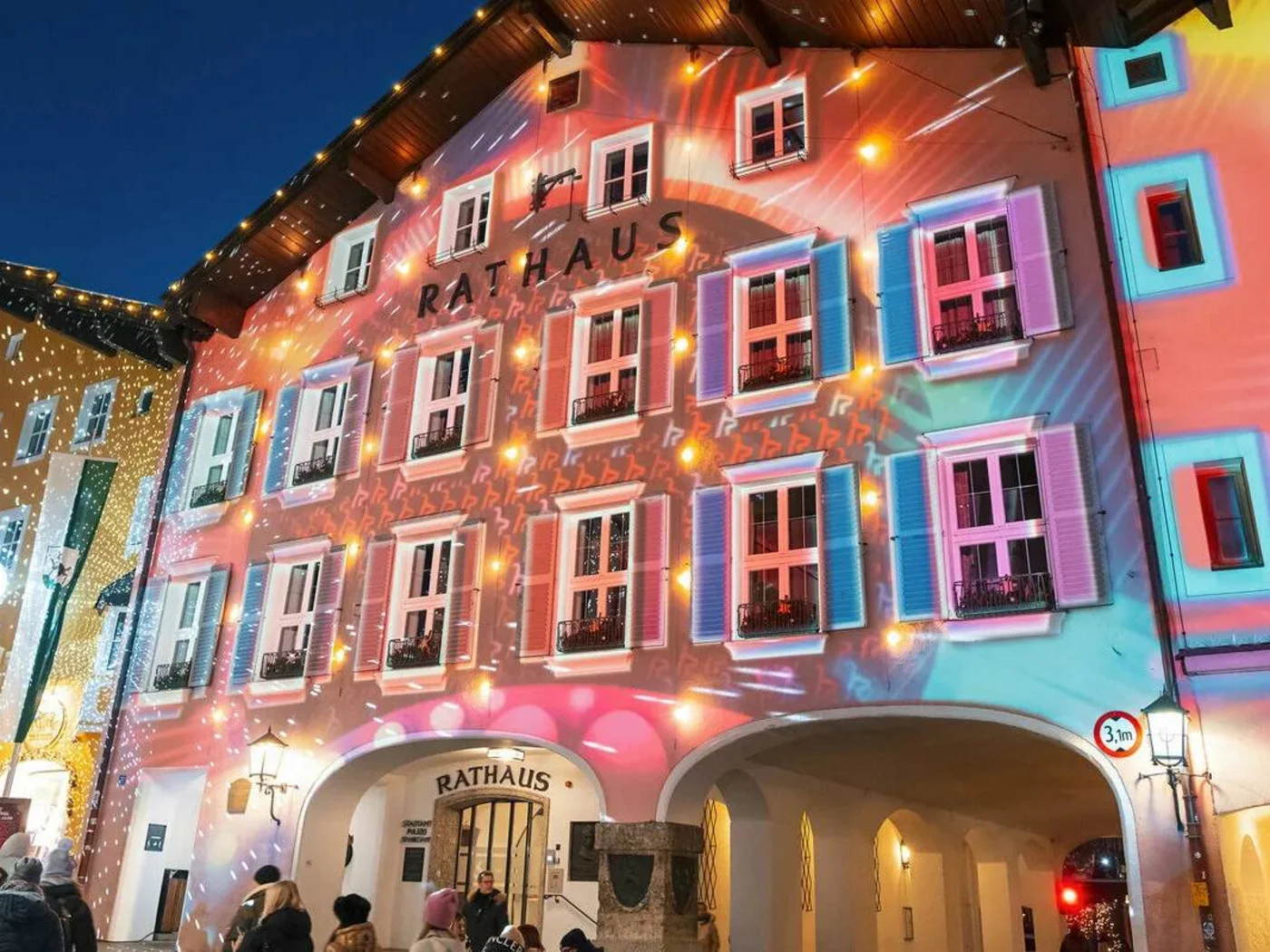 Illuminated town hall building with colorful lights and people in the evening