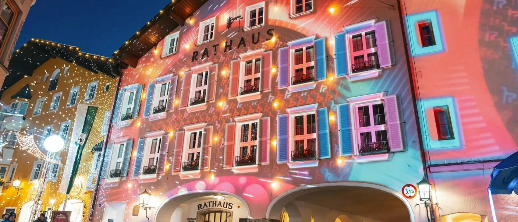 Mit Kitzbühel ins neue Jahr Beleuchtetes Rathausgebäude mit bunten Lichtern und Menschen am Abend