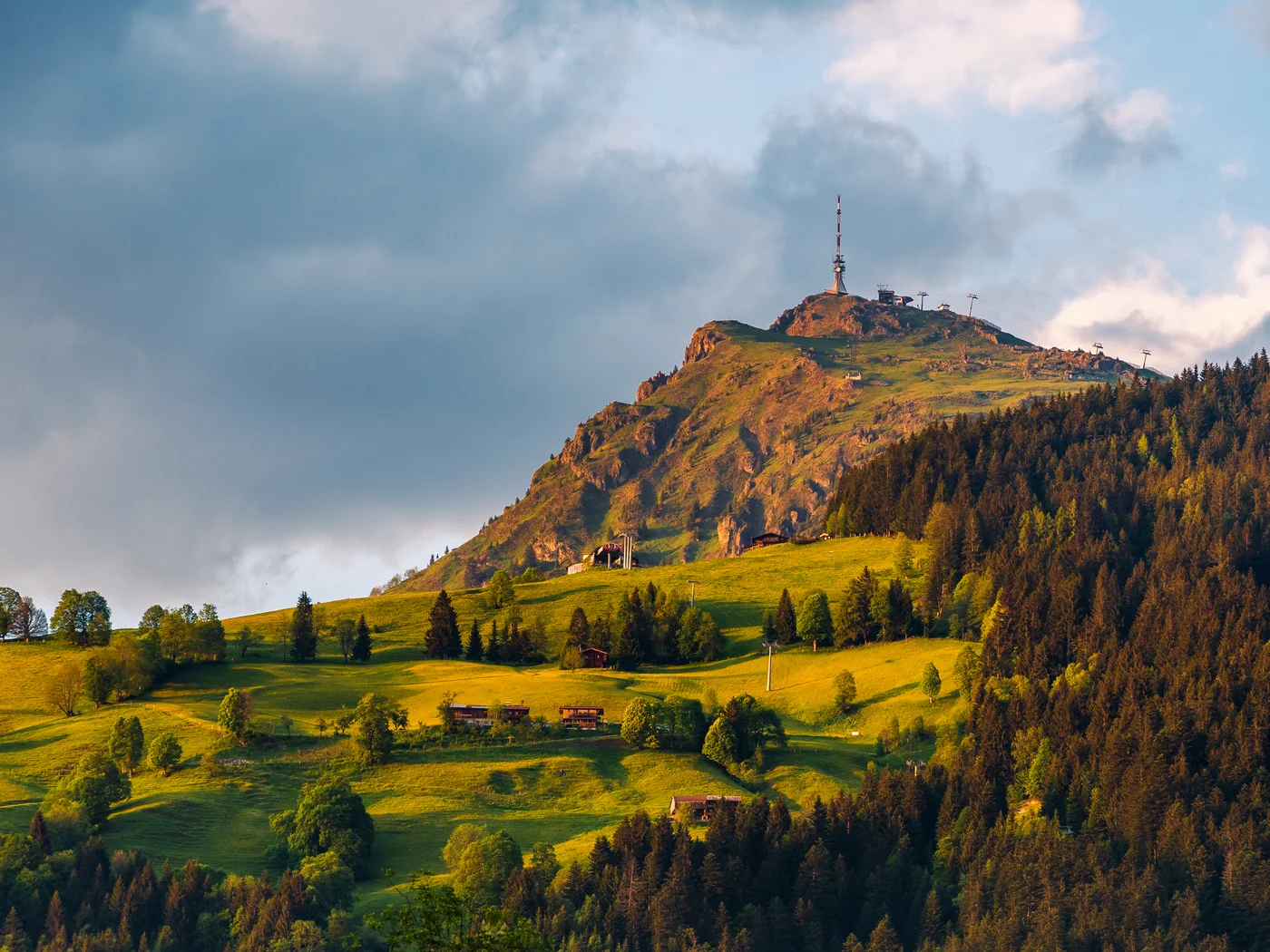 Berg mit Sendeantenne und grüner Wiese im Vordergrund bei bewölktem Himmel