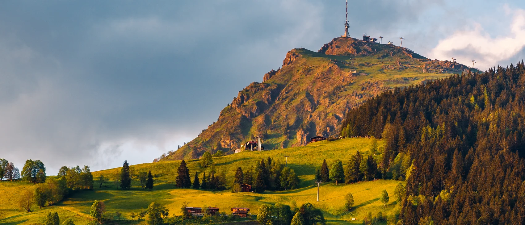 Berg mit Sendeantenne und grüner Wiese im Vordergrund bei bewölktem Himmel
