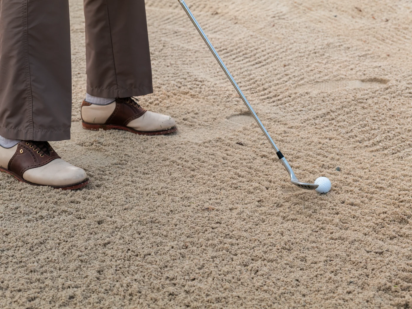 Golfschläger und Ball in einem Sandbunker mit golfer Schuhen