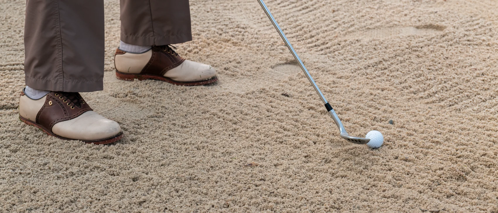 Golfschläger und Ball in einem Sandbunker mit golfer Schuhen