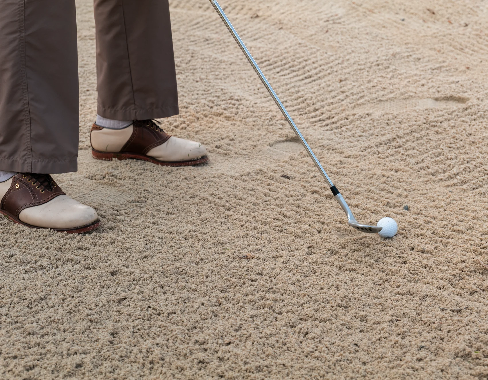 Golfschläger und Ball in einem Sandbunker mit golfer Schuhen