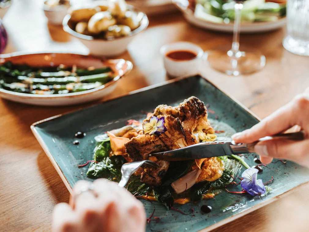 Person cutting an artistically plated dish on a blue plate