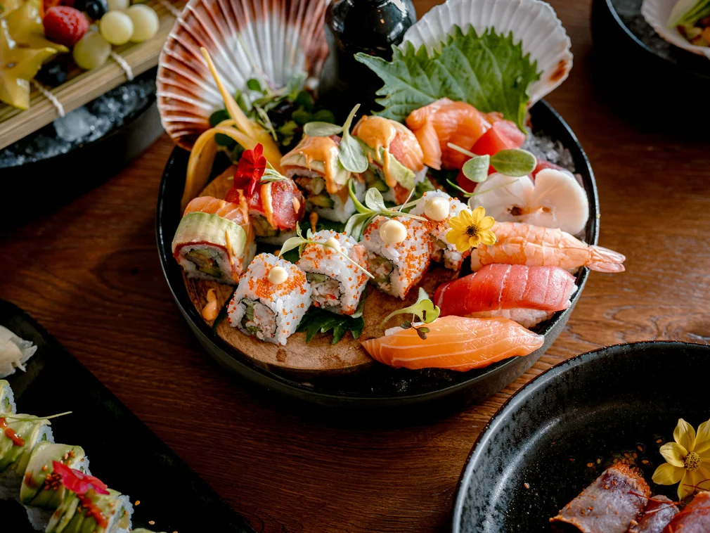 Assorted sushi and sashimi on a black plate with garnishes and flowers