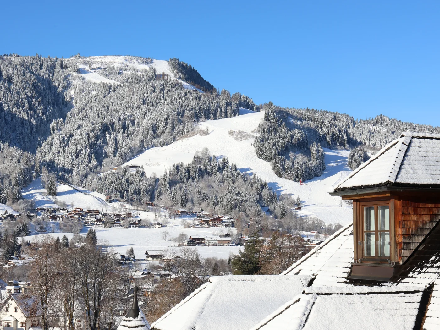 Schneebedeckte Dächer mit Blick auf verschneite Berge und blauen Himmel