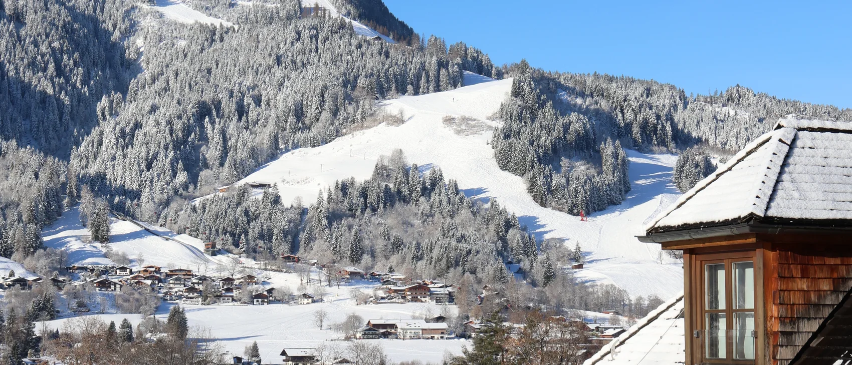 Schneebedecktes Dach mit Blick auf verschneite Berge und blauen Himmel