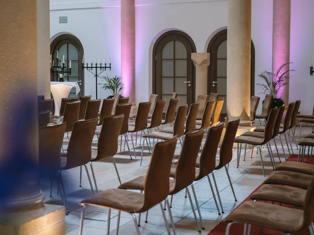 Rows of empty chairs in a room with columns and purple lighting
