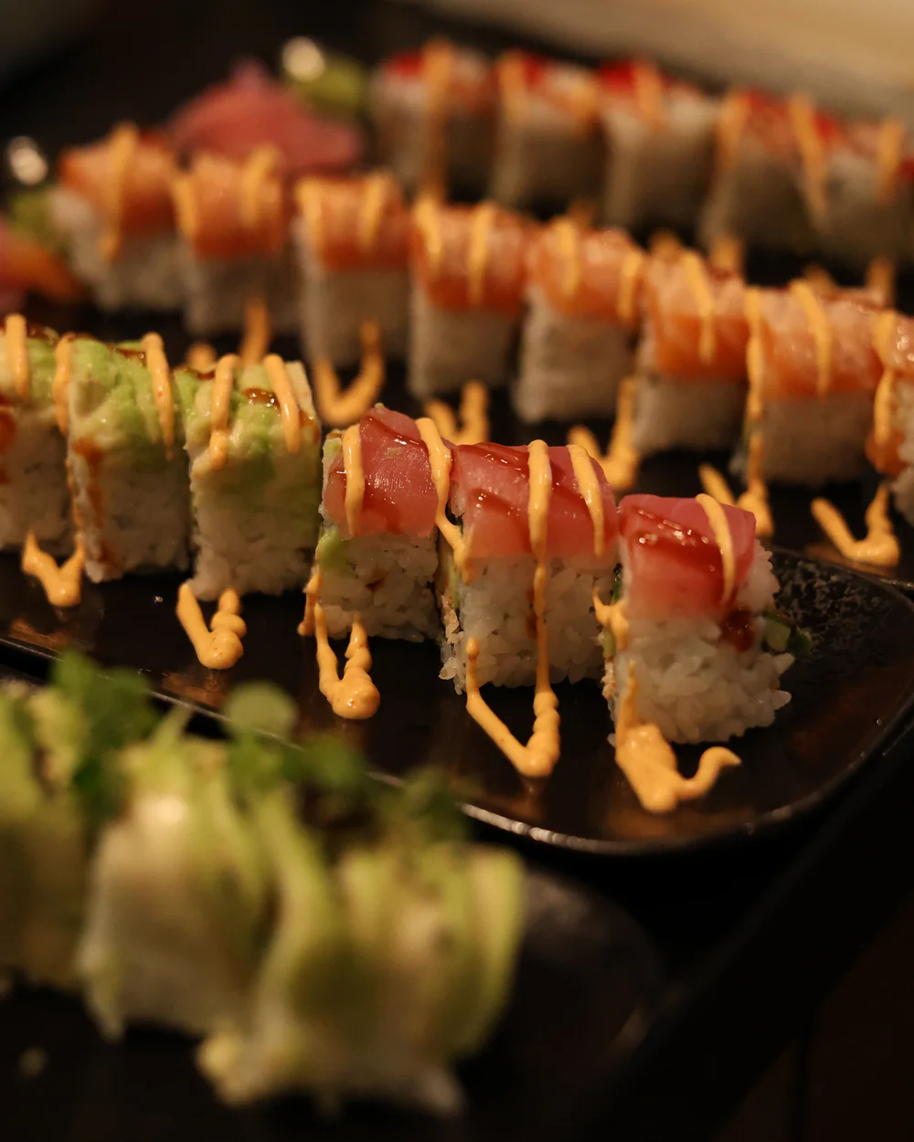 Verschiedene Sushi-Rollen mit Sauce auf schwarzem Teller