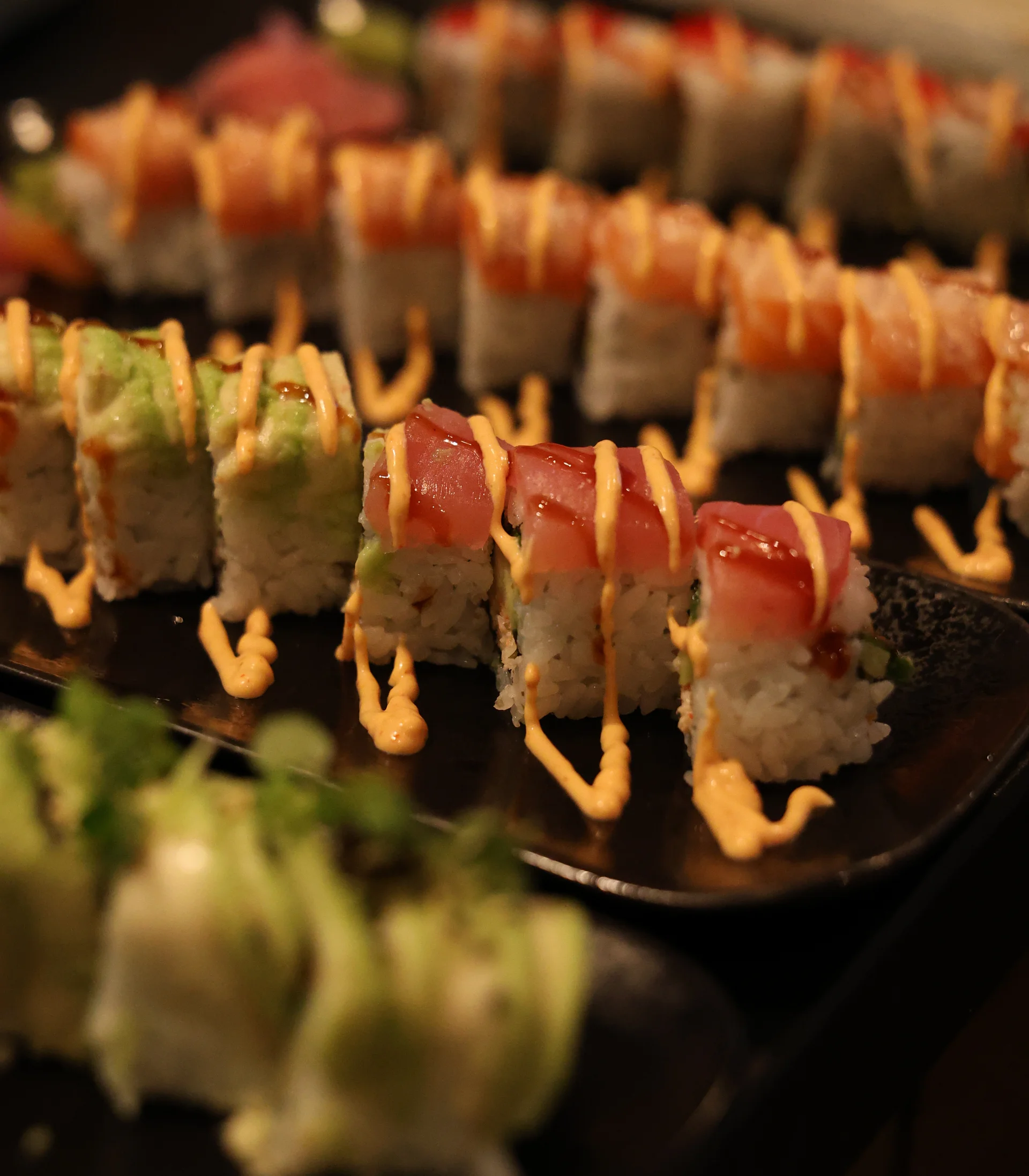 Verschiedene Sushi-Rollen mit Sauce auf schwarzem Teller