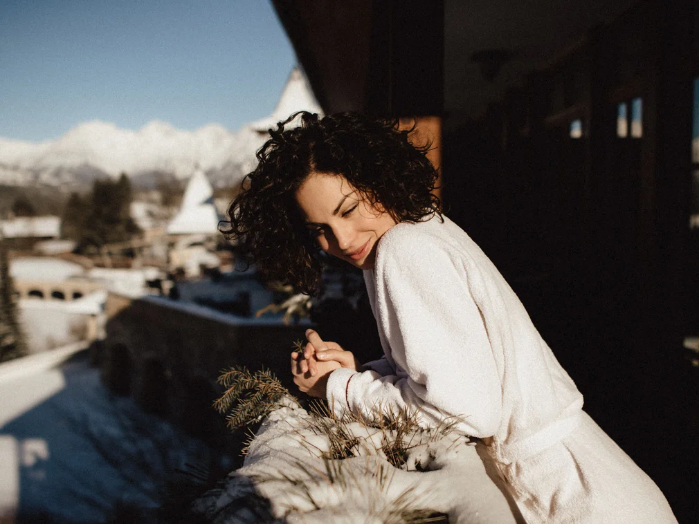 Woman in bathrobe enjoying winter sun on balcony with mountain view