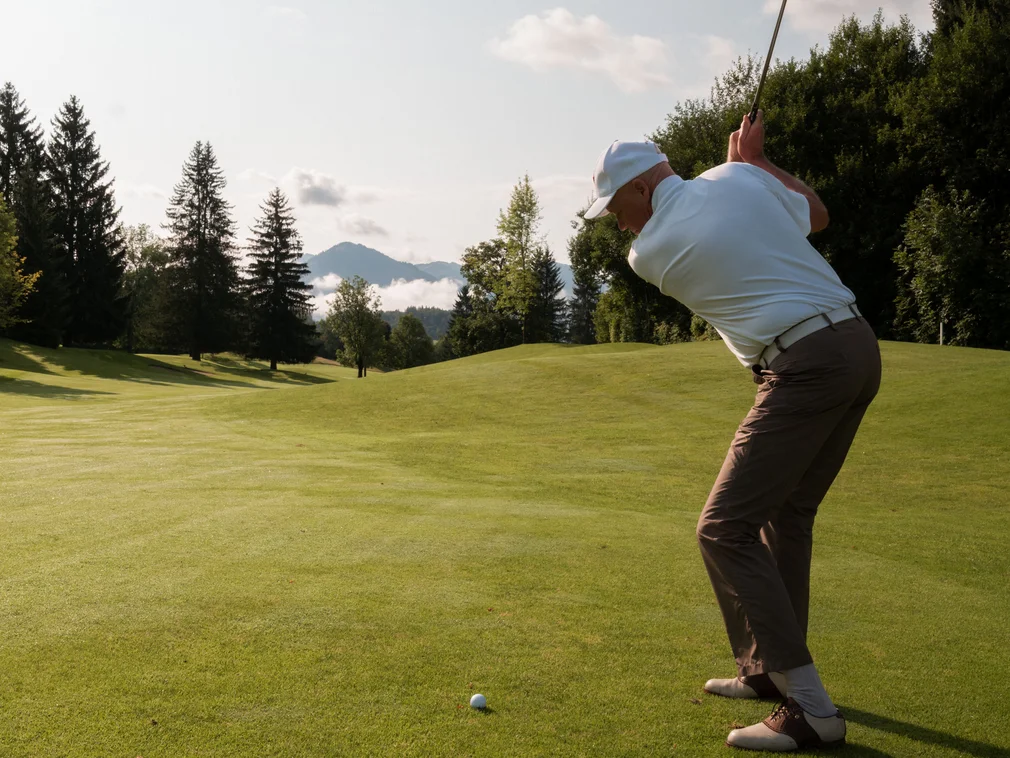 Man playing golf on sunny course with mountains in the background