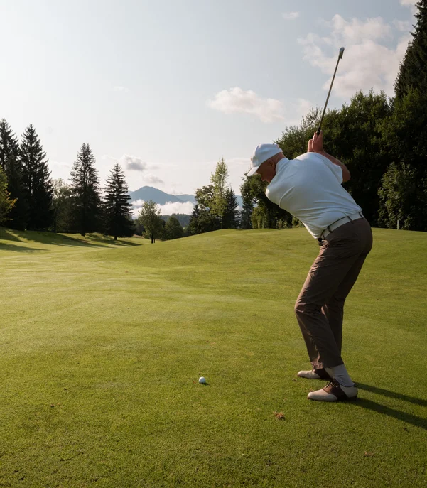 Mann beim Golfspielen auf einem sonnigen Golfplatz mit Bergen im Hintergrund