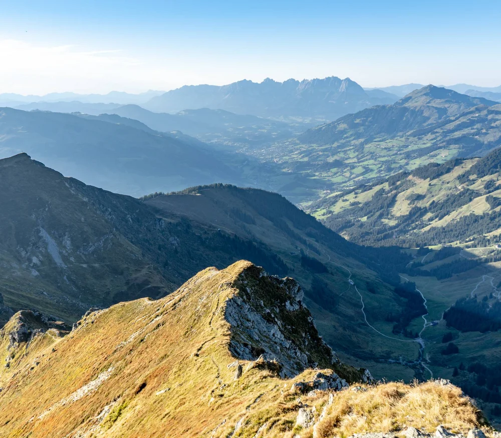 Blick auf sonnige Berggipfel und ein Tal in den Alpen bei klarem Himmel.