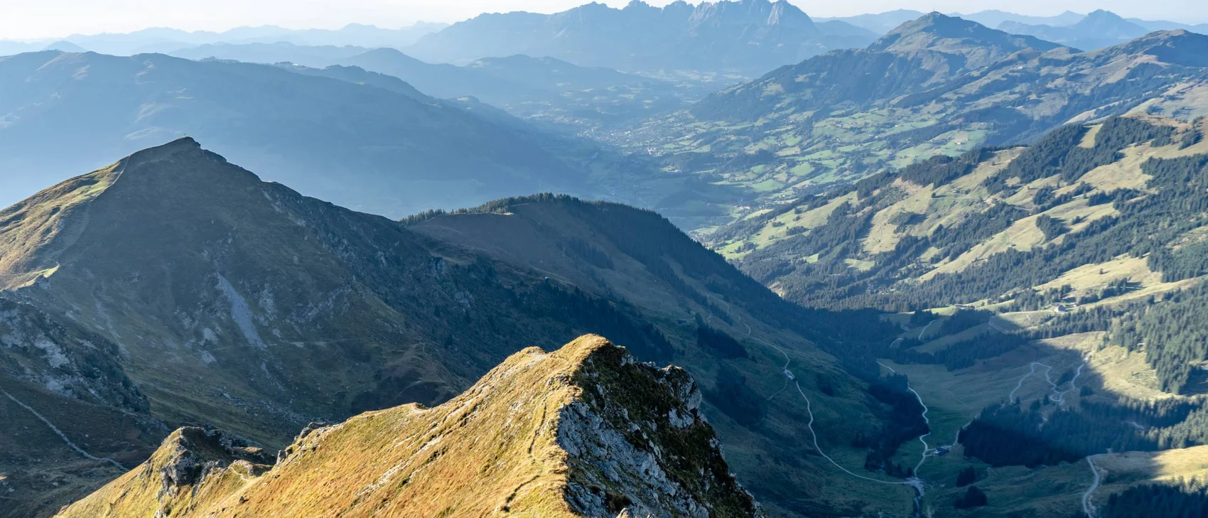 Blick auf sonnige Berggipfel und ein Tal in den Alpen bei klarem Himmel.