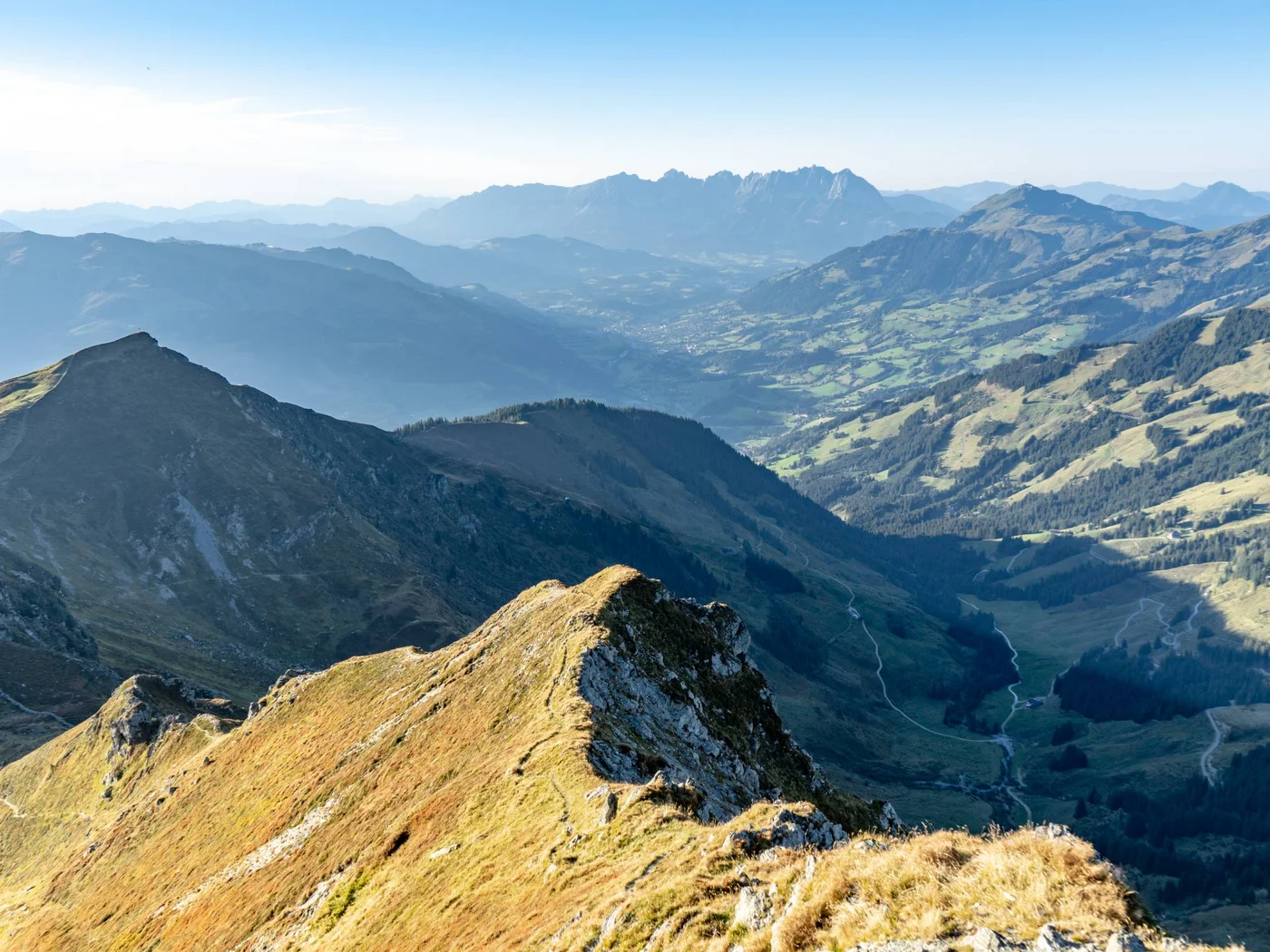Blick auf sonnige Berggipfel und ein Tal in den Alpen bei klarem Himmel.