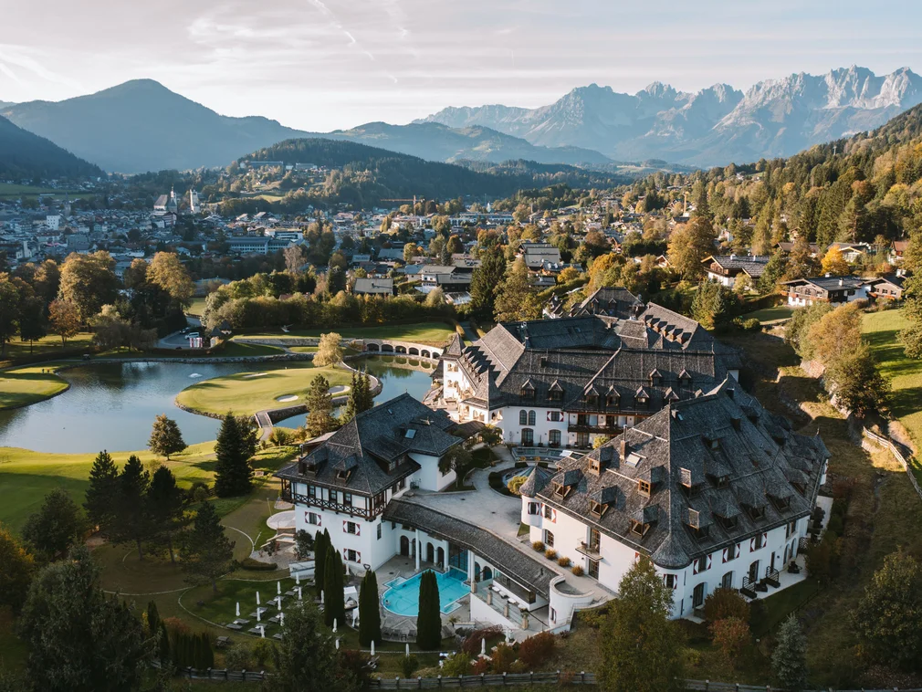 Aerial view of a mountain hotel with golf course and village in the background