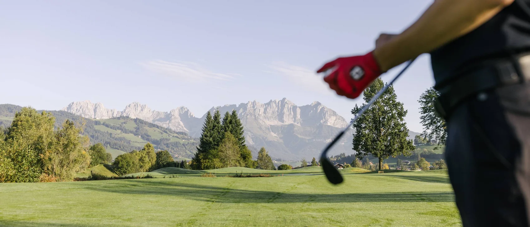 Golfer mit rotem Handschuh auf einem grünen Golfplatz vor Bergkulisse