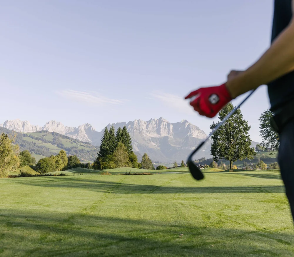 Golfista con guanto rosso su campo da golf verde con montagne sullo sfondo