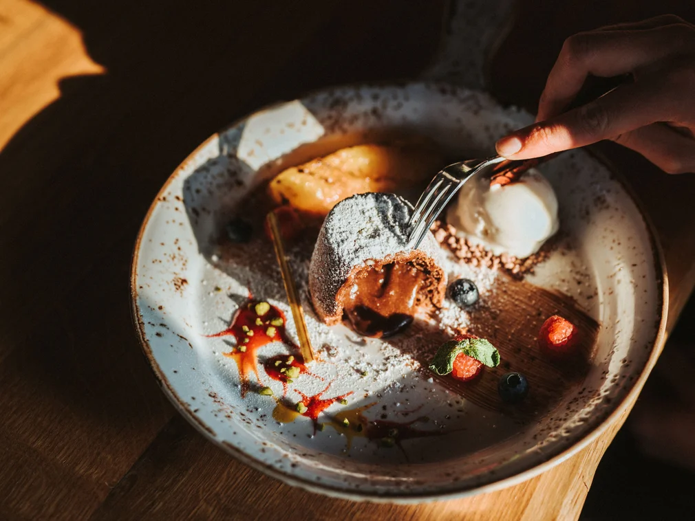 Hand holding fork, taking warm chocolate cake with berries and ice cream from plate