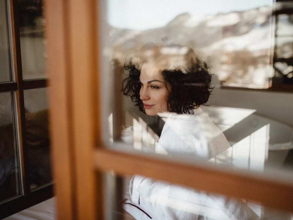 Woman in white robe looking thoughtfully out the window