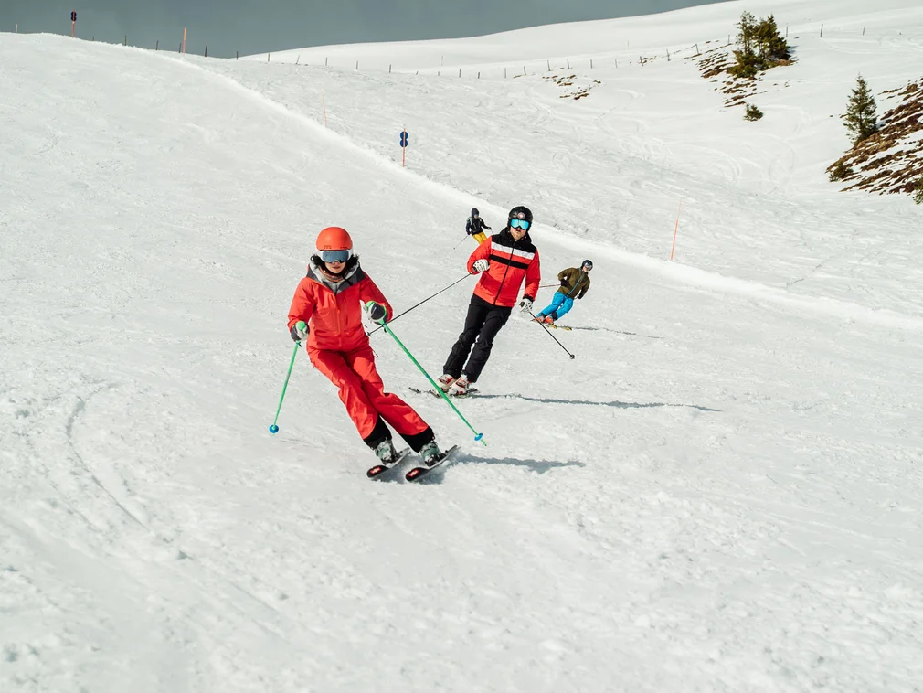 Several skiers in red and blue outfits on a snowy ski slope