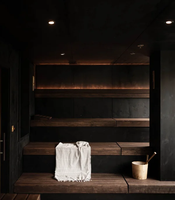 Modern dark sauna room with wooden benches and sauna bucket