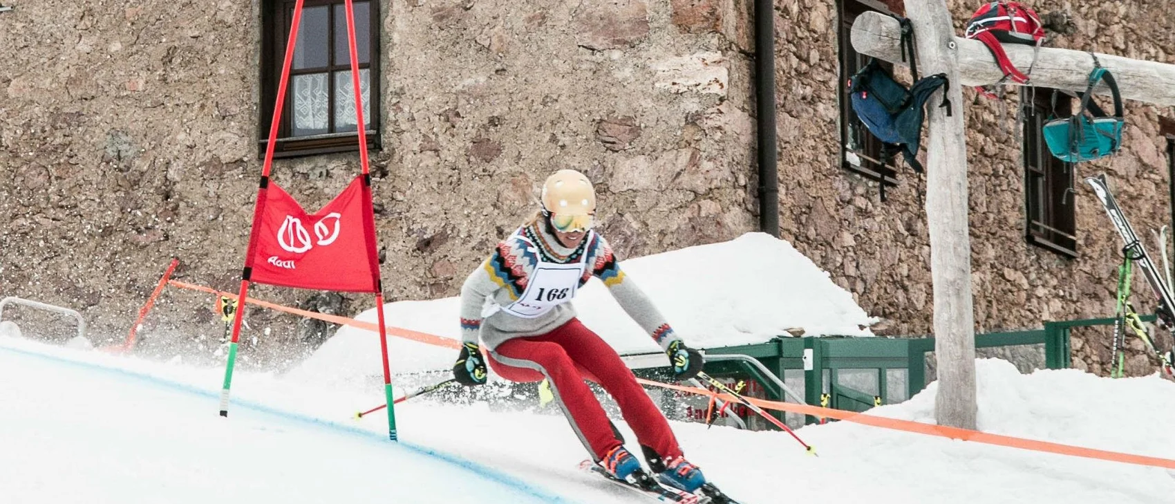Skifahrer bei einem Rennen auf verschneiter Strecke vor einem Steinbau