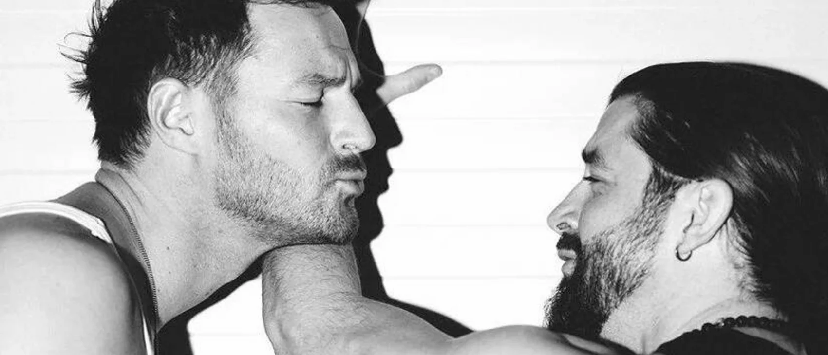 Close-up of two men, one kissing the other's arm