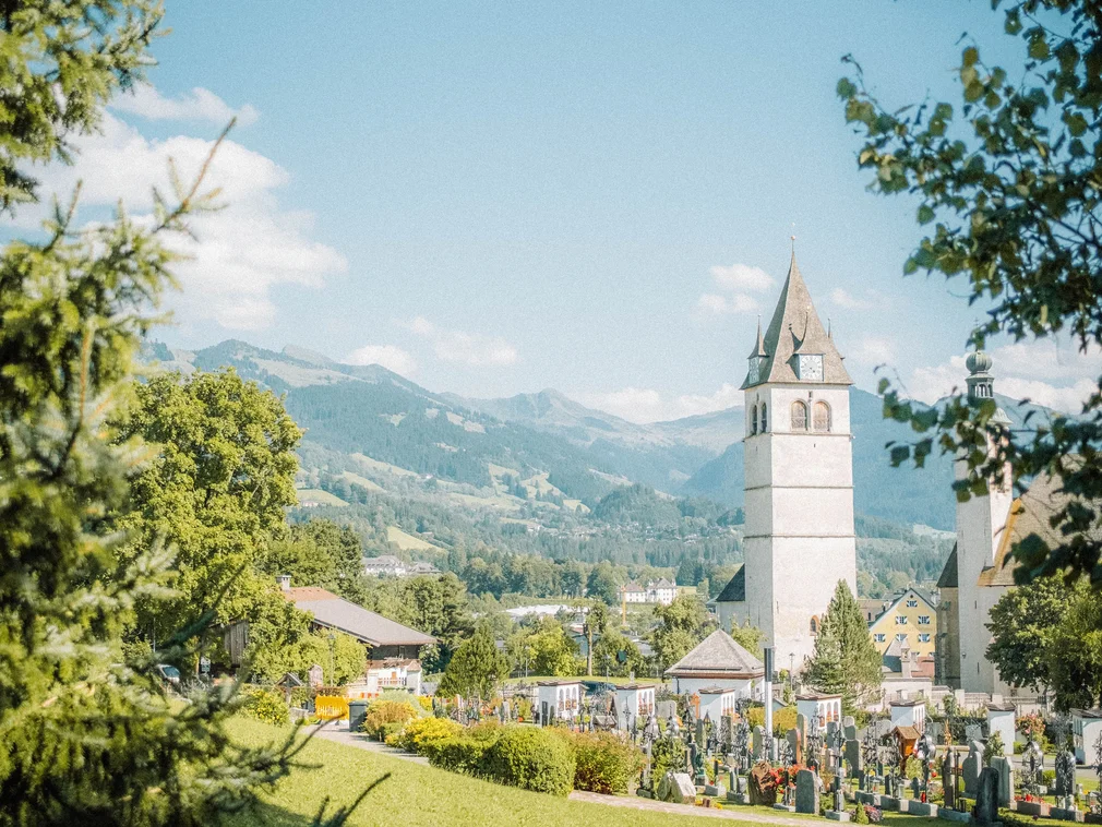 Church tower and cemetery in green landscape with mountains in the background