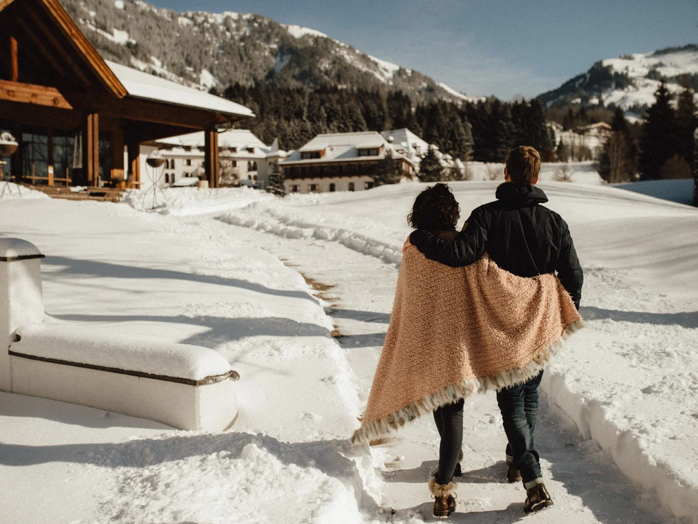 Couple wrapped in blanket walking on snowy mountain path