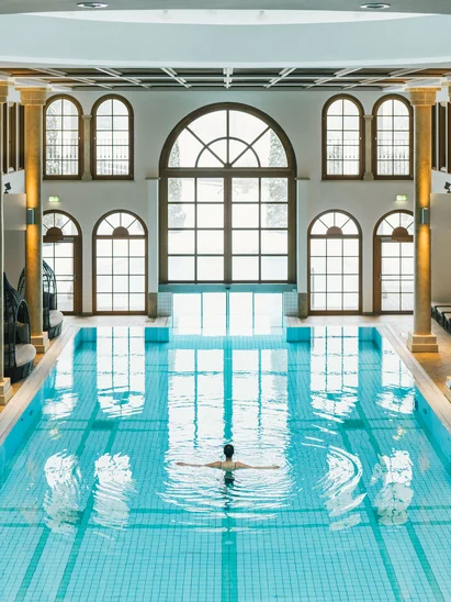 Flitterwochen im Hotel in Österreich | Schlosshotel Kitzbühel Innenaufnahme eines Schwimmbads mit Säulen und einer Person im Wasser