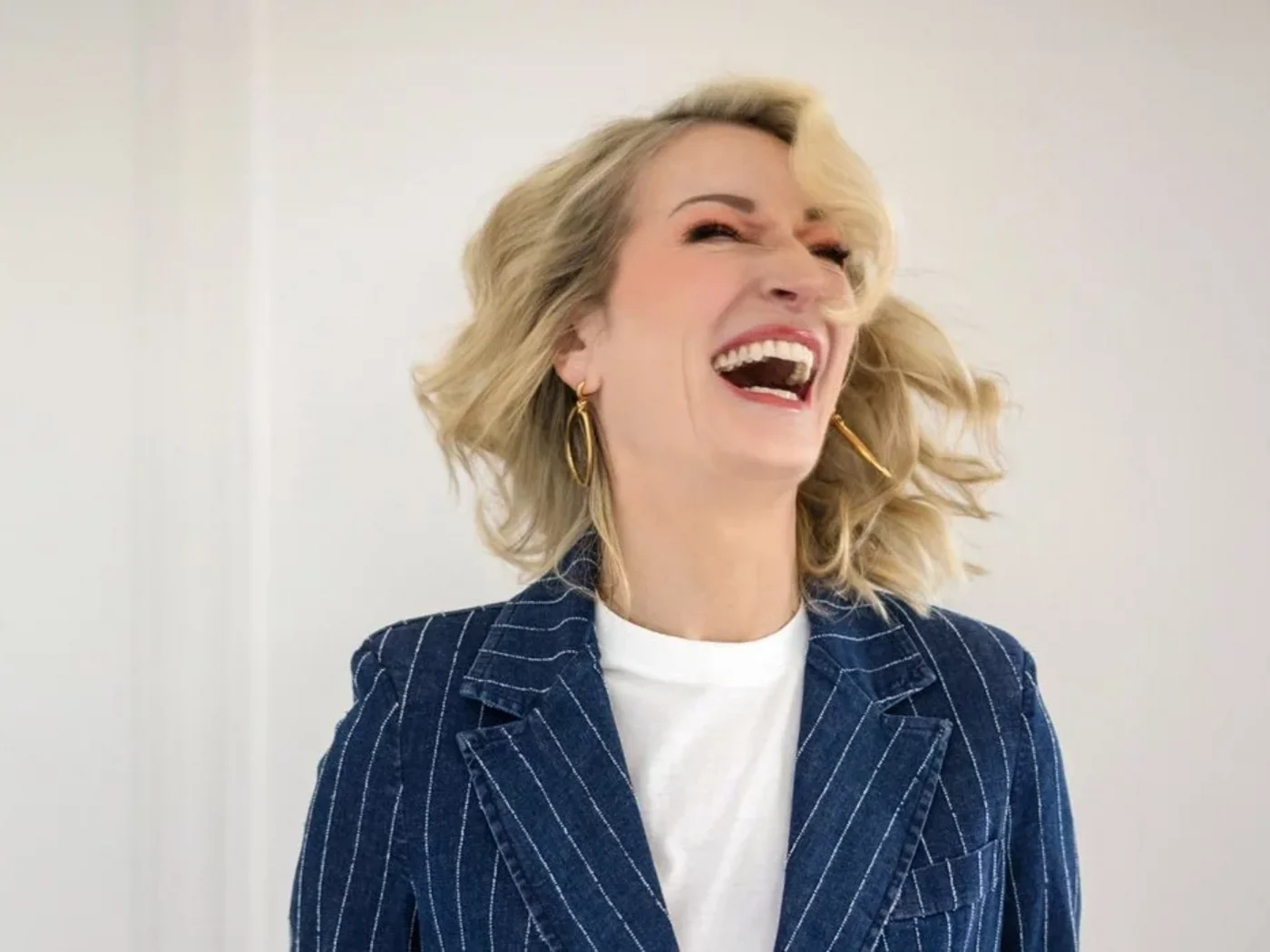 Frau mit blonden Haaren lacht laut in einem gestreiften Blazer