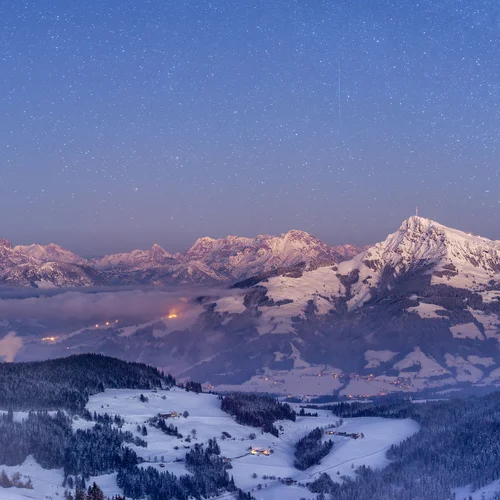 In Kitzbühel: the ski hotel of your dreams Snow-covered mountains at night with starry sky and lights in the valley