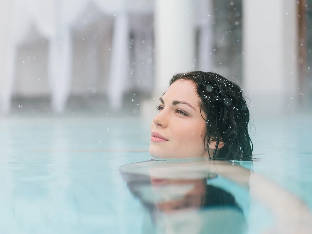 Woman relaxing in water with falling snow in the background