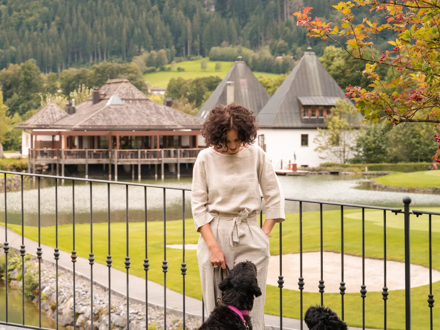 Frau streichelt zwei schwarze Hunde vor Berglandschaft und Häusern
