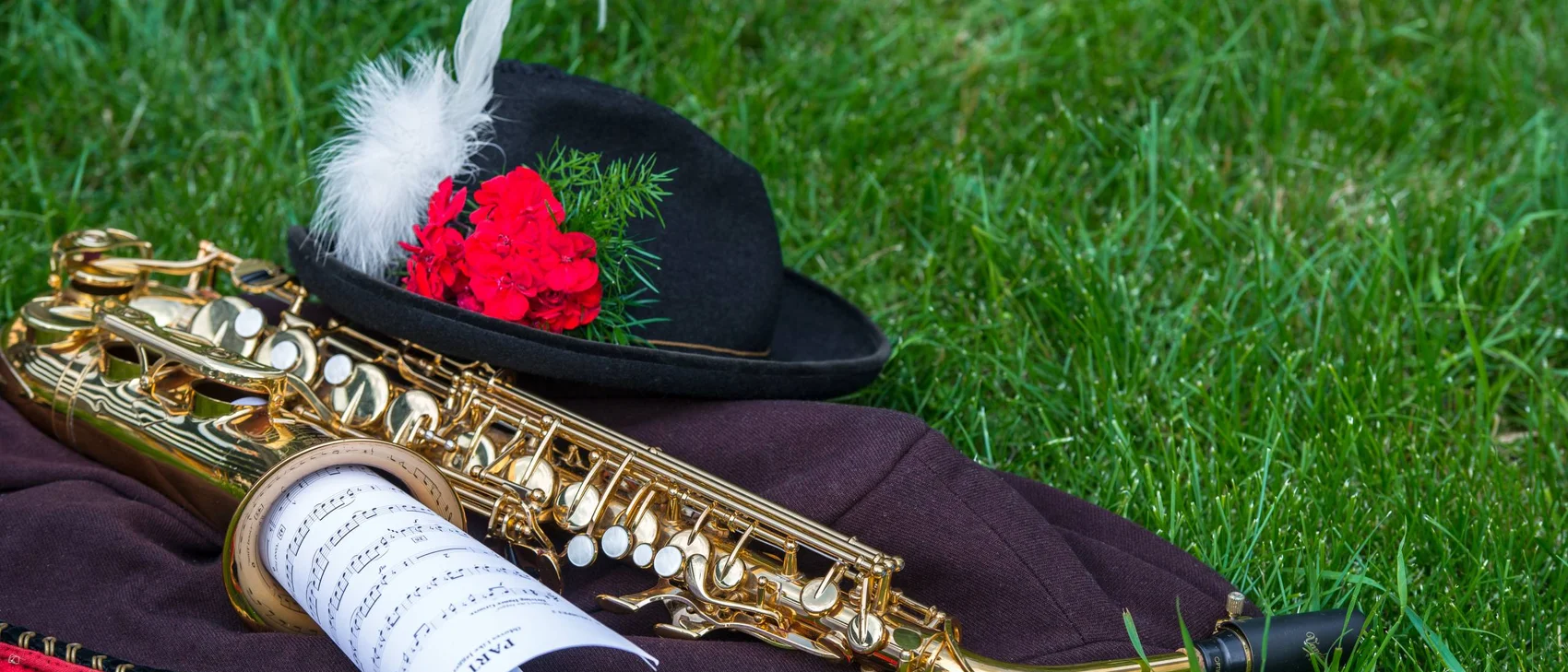 Saxophon, Notenblatt und Hut mit Feder und roten Blumen auf Gras
