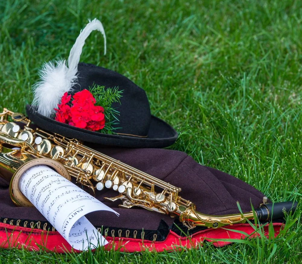 Sassofono, spartiti e cappello con piuma e fiori rossi sull'erba